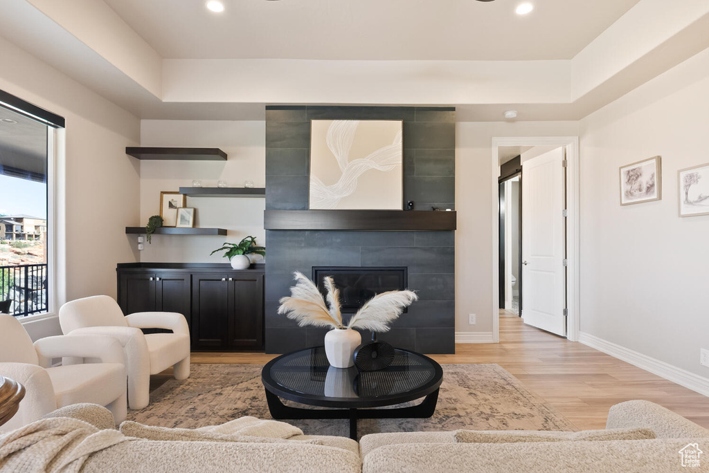 Living room with light wood-style flooring, baseboards, a tiled fireplace, recessed lighting, and a raised ceiling