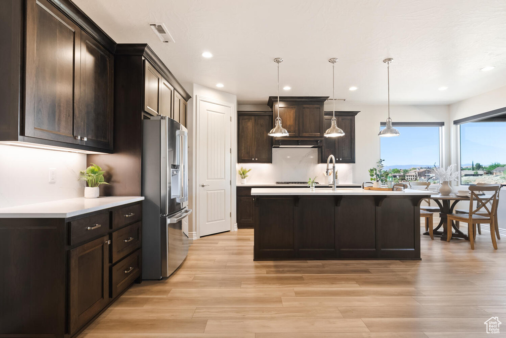 Kitchen with stainless steel refrigerator with ice dispenser, a kitchen breakfast bar, light countertops, light wood-style flooring, and recessed lighting