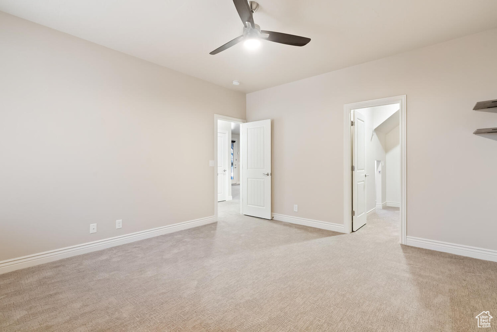Unfurnished bedroom with light carpet, baseboards, ensuite bath, and ceiling fan