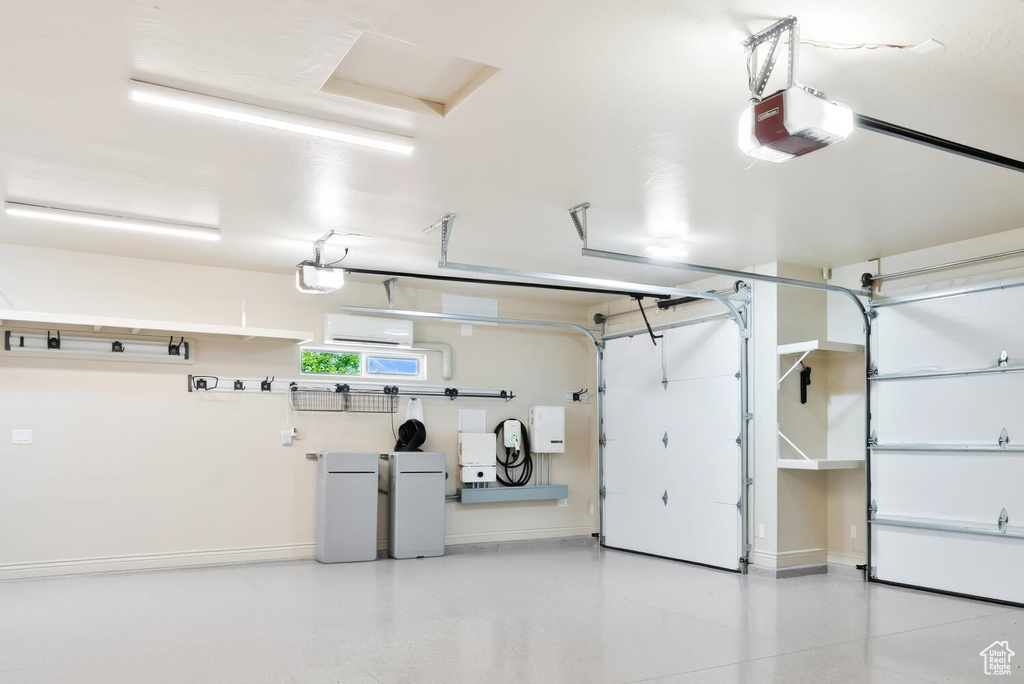 Garage with a garage door opener, baseboards, and a wall mounted AC