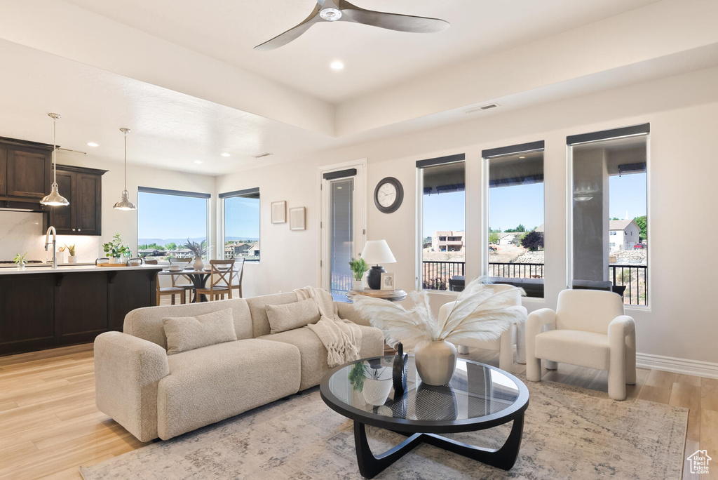 Living area with recessed lighting, light wood-type flooring, a ceiling fan, baseboards, and a tray ceiling