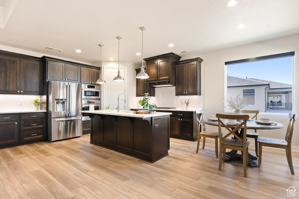 Kitchen with appliances with stainless steel finishes, light countertops, dark brown cabinets, light wood-type flooring, and recessed lighting
