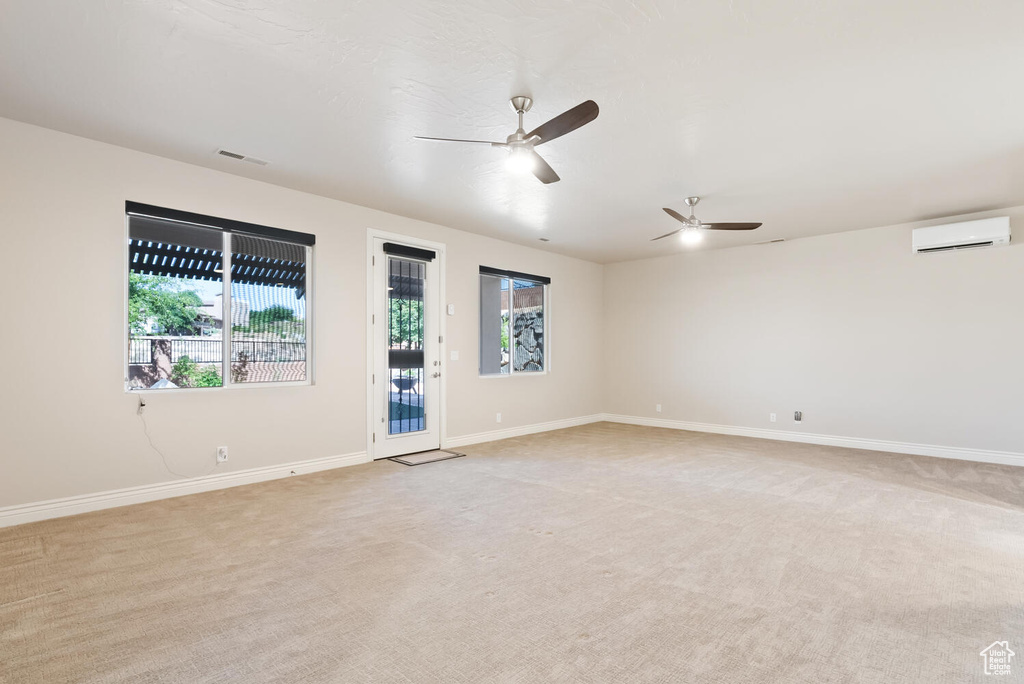 Unfurnished room featuring healthy amount of natural light, a wall mounted AC, light carpet, and a ceiling fan