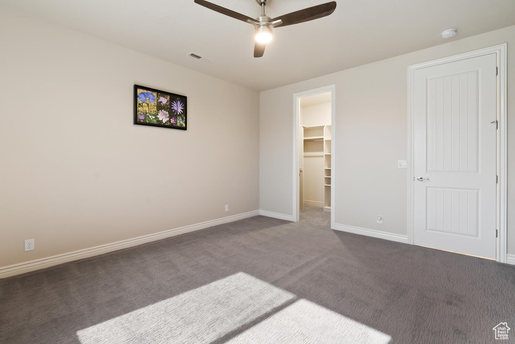 Unfurnished bedroom with a spacious closet, dark carpet, baseboards, a ceiling fan, and a closet