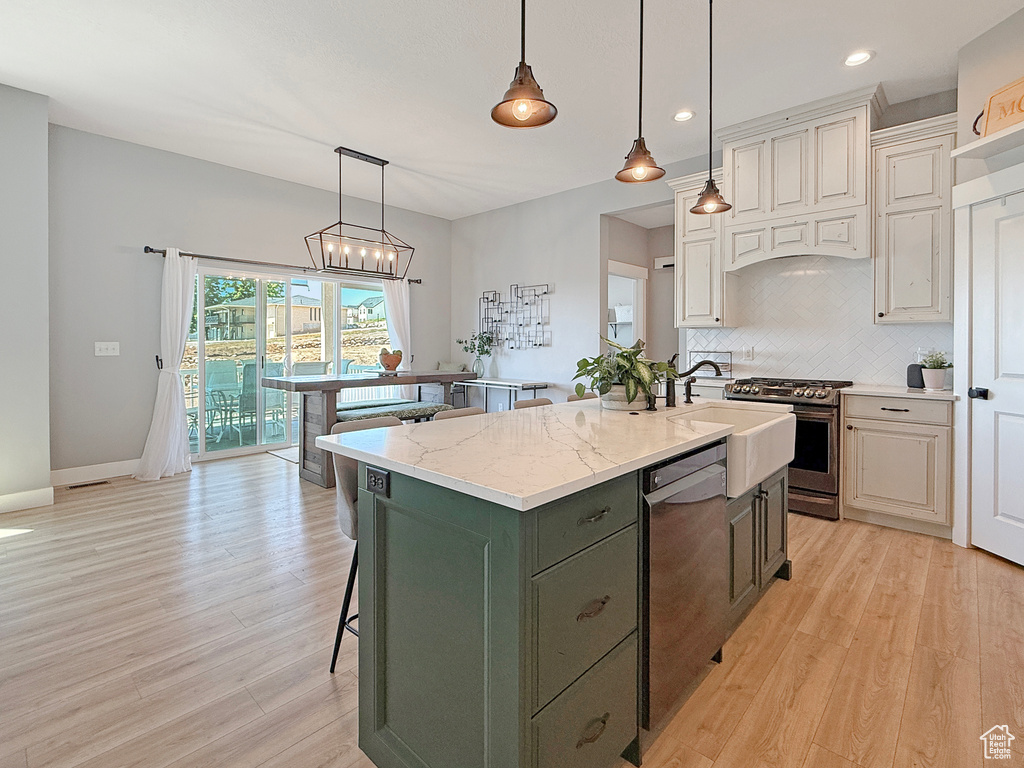 Kitchen featuring dishwasher, stainless steel gas stove, decorative backsplash, an island with sink, and light wood finished floors