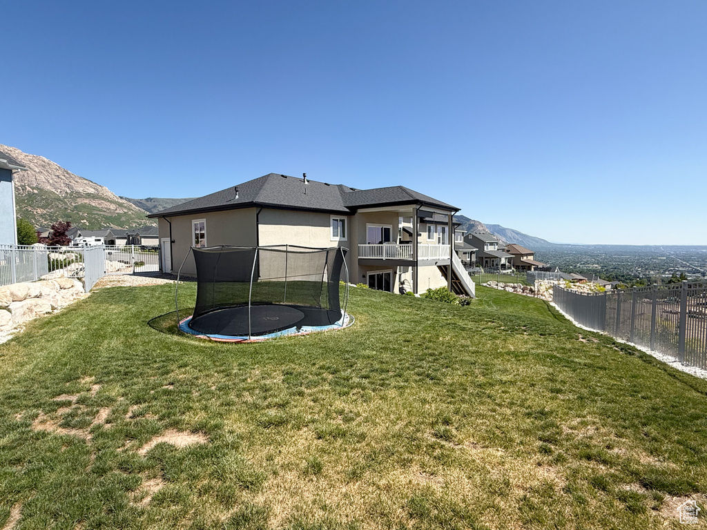 Rear view of house with a trampoline, a mountain view, stucco siding, and stairway