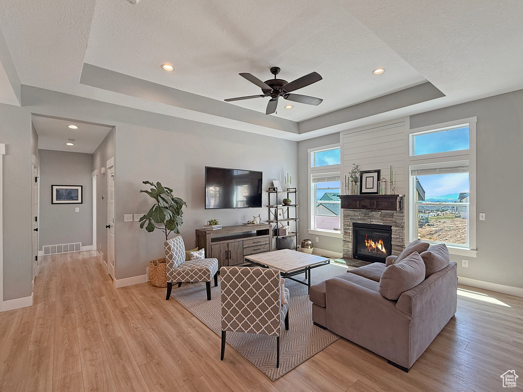 Living room with a raised ceiling, baseboards, light wood finished floors, a ceiling fan, and a fireplace