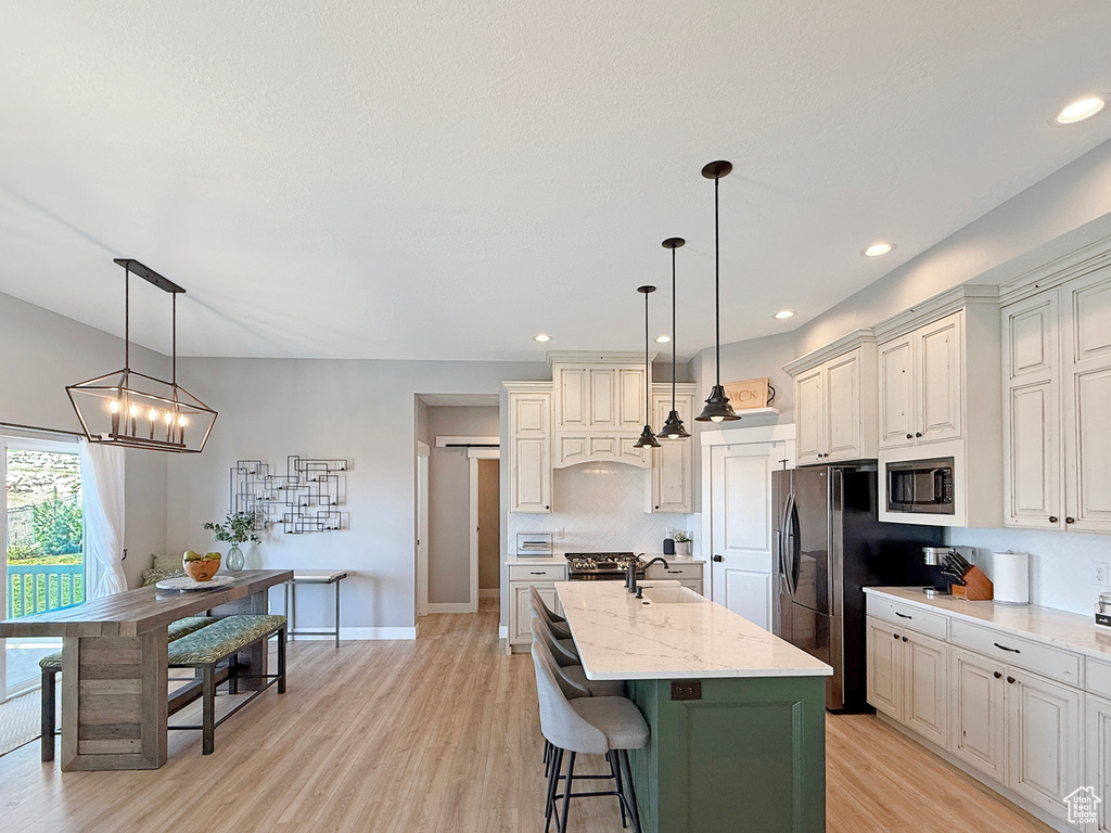 Kitchen with appliances with stainless steel finishes, a sink, light wood-style floors, a center island with sink, and light stone counters