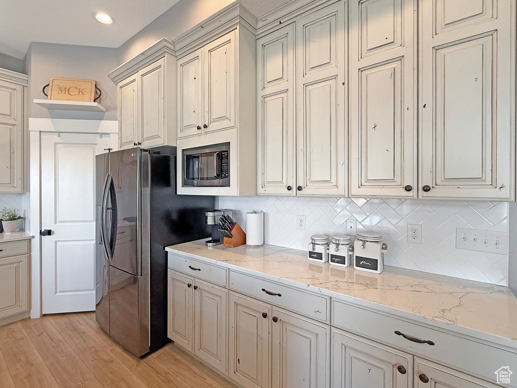 Kitchen featuring built in microwave, tasteful backsplash, freestanding refrigerator, light wood-style floors, and light stone counters