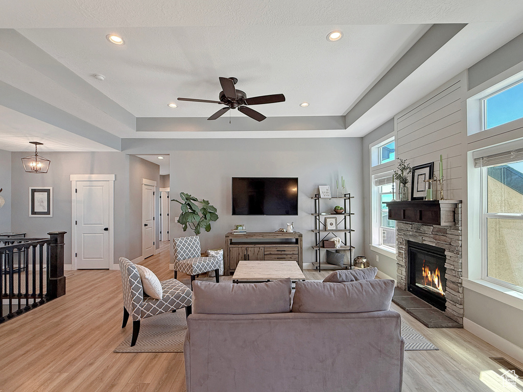 Living room featuring light wood-style floors, baseboards, a fireplace, a tray ceiling, and recessed lighting