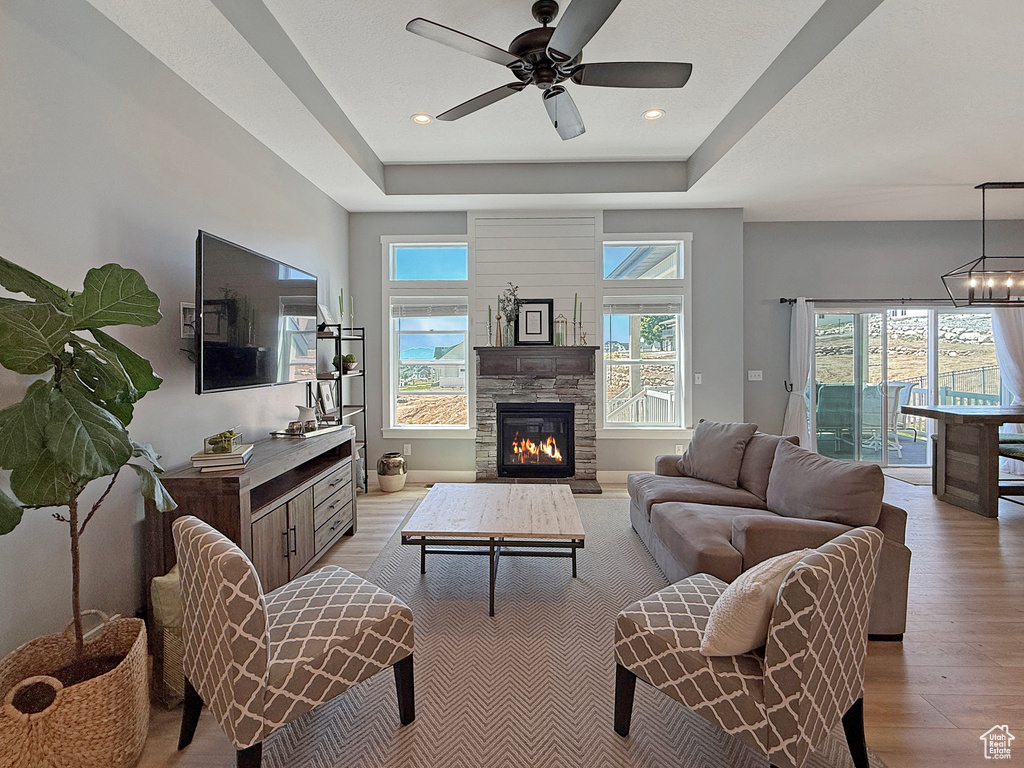 Living area with light wood finished floors, ceiling fan, a tray ceiling, a fireplace, and recessed lighting