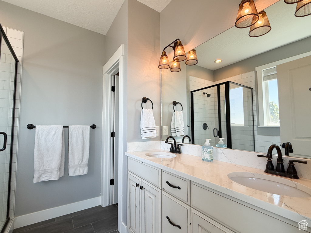 Bathroom featuring a stall shower, double vanity, baseboards, wood finished floors, and a textured ceiling