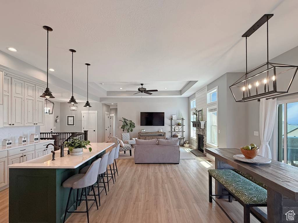 Kitchen featuring a tray ceiling, light countertops, light wood-type flooring, a kitchen bar, and ceiling fan