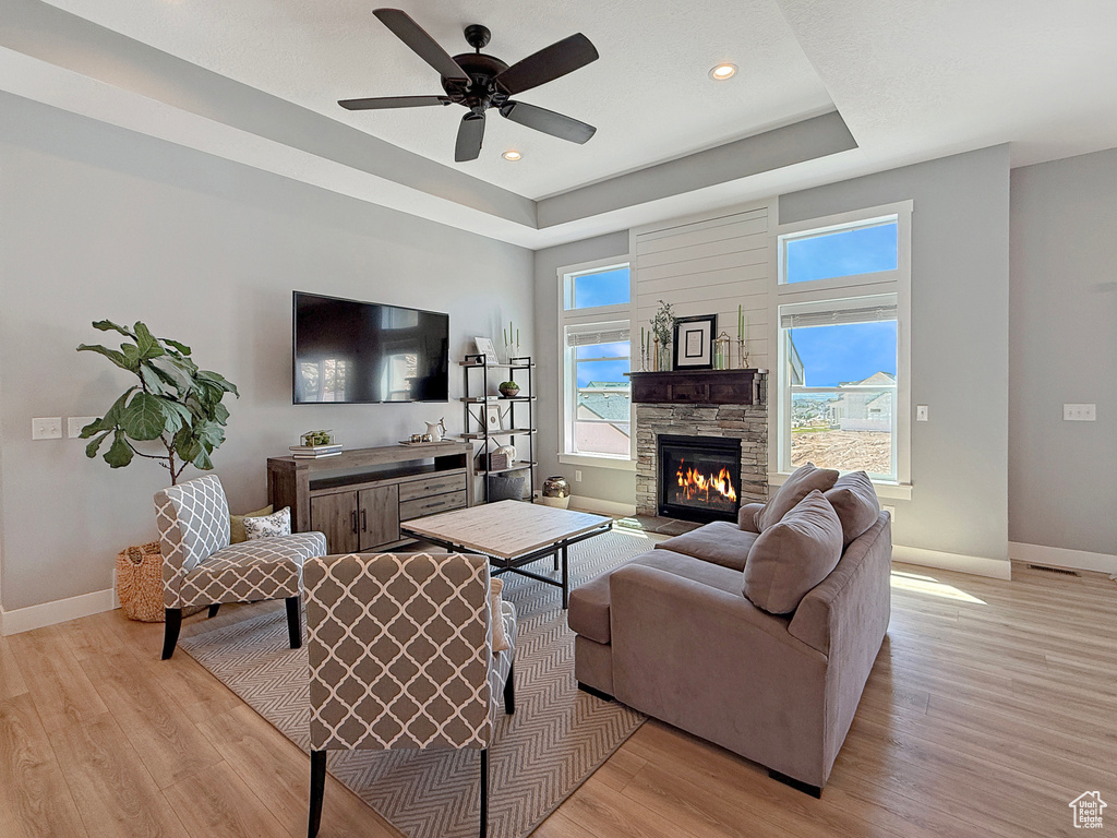 Living area with baseboards, a tray ceiling, light wood-type flooring, a fireplace, and recessed lighting