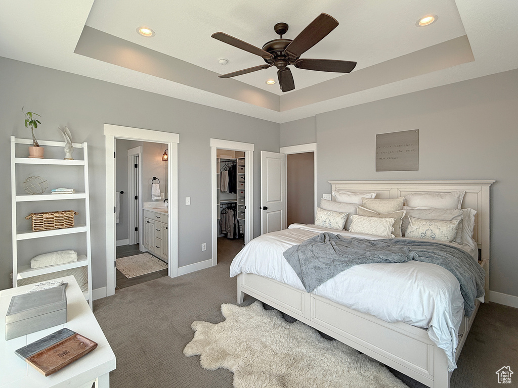 Carpeted bedroom with a raised ceiling, a spacious closet, baseboards, recessed lighting, and ensuite bathroom