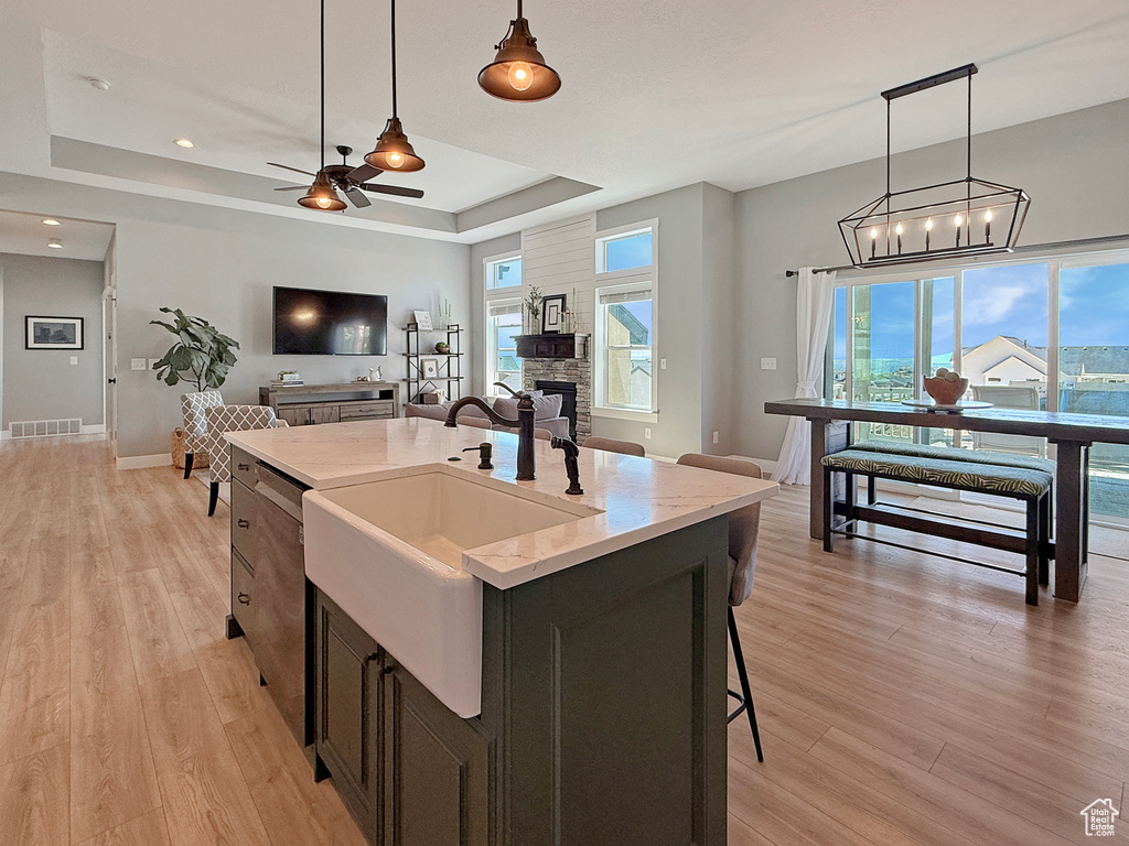 Kitchen featuring a raised ceiling, a sink, open floor plan, a ceiling fan, and pendant lighting