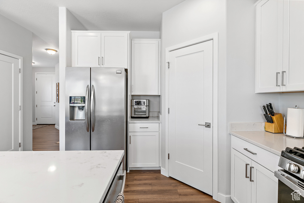 Kitchen with stainless steel refrigerator with ice dispenser, dark wood-type flooring, and white cabinetry