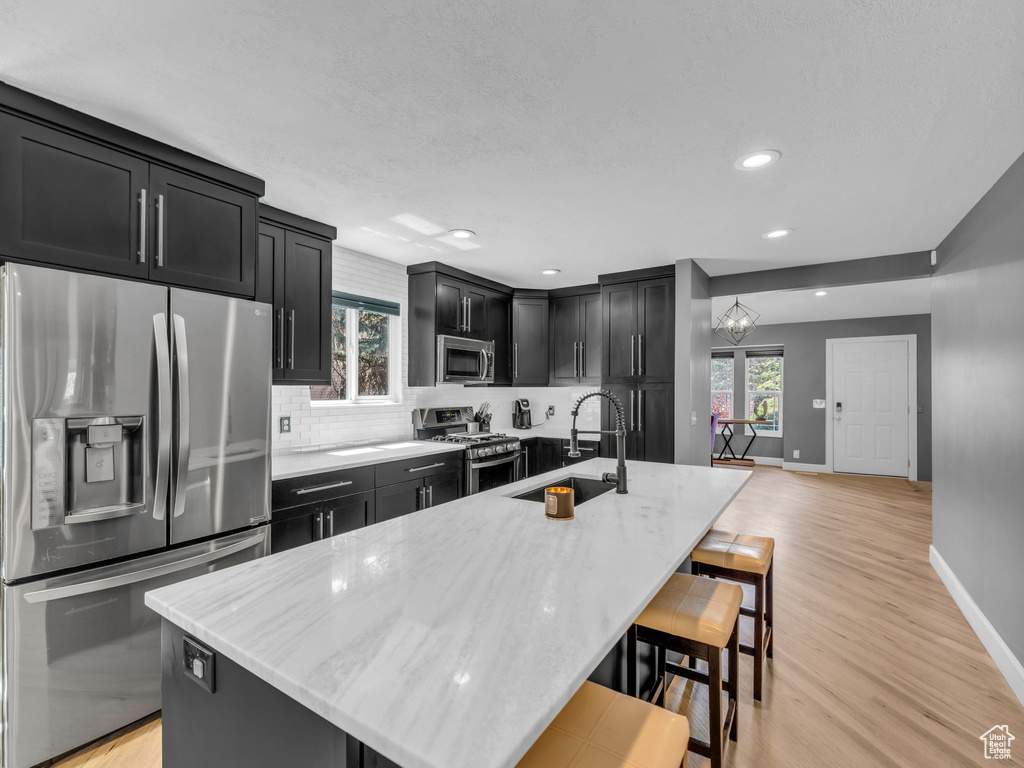 Kitchen featuring stainless steel appliances, a sink, dark cabinets, baseboards, and decorative backsplash