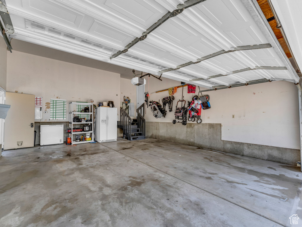 Garage featuring a garage door opener and white refrigerator with ice dispenser