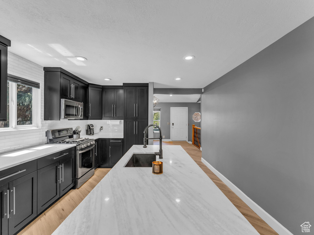 Kitchen with stainless steel appliances, a sink, dark cabinets, baseboards, and recessed lighting