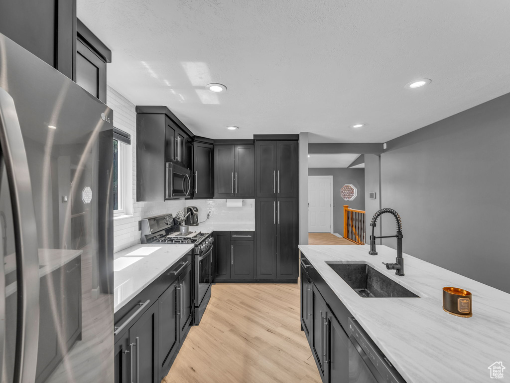 Kitchen featuring appliances with stainless steel finishes, a sink, light wood-style floors, decorative backsplash, and dark cabinetry