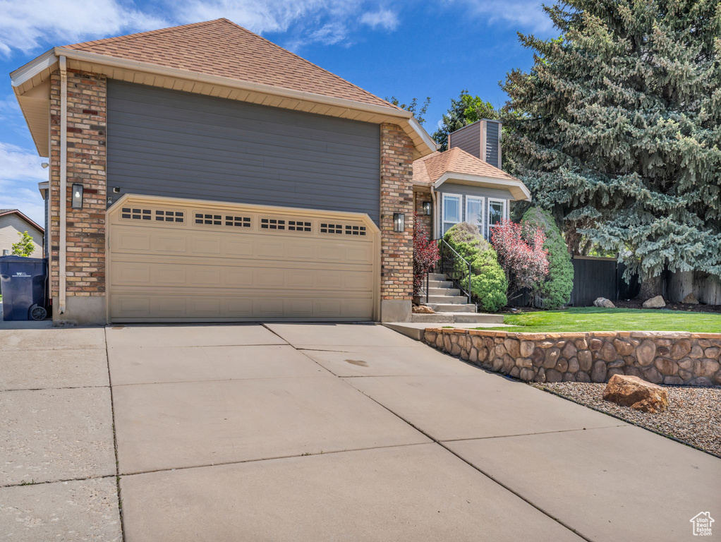 View of front facade with a shingled roof, brick siding, a front lawn, and driveway