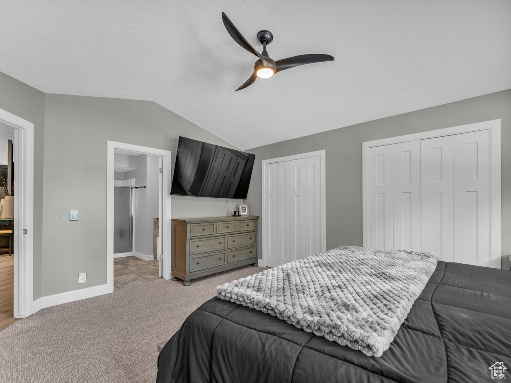 Bedroom featuring vaulted ceiling, two closets, light carpet, baseboards, and a ceiling fan