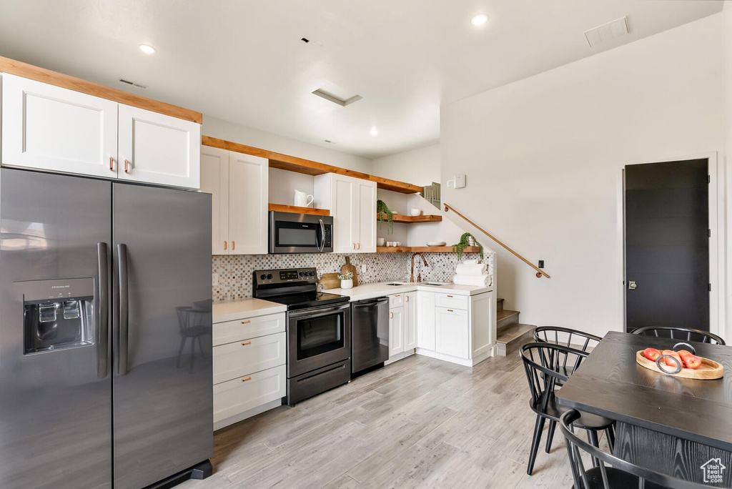 Kitchen with stainless steel appliances, open shelves, light countertops, tasteful backsplash, and white cabinetry