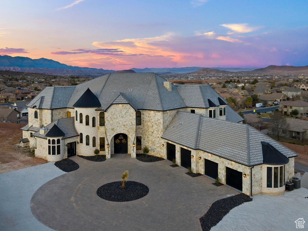 French provincial home with stone siding, curved driveway, a mountain view, an attached garage, and a high end roof