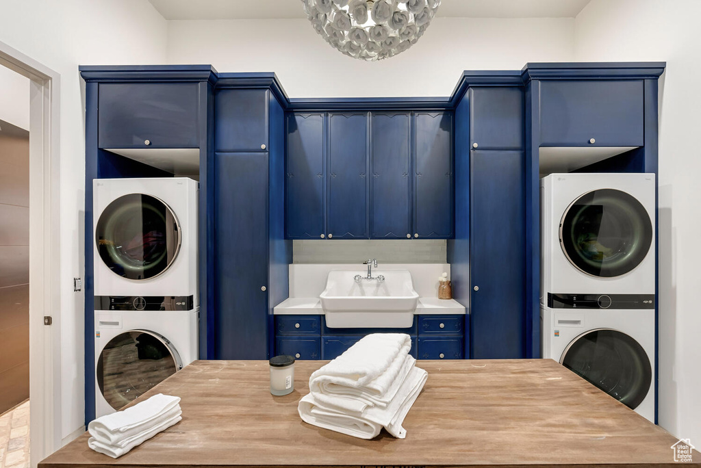 Laundry area featuring stacked washing machine and dryer, cabinet space, and a chandelier