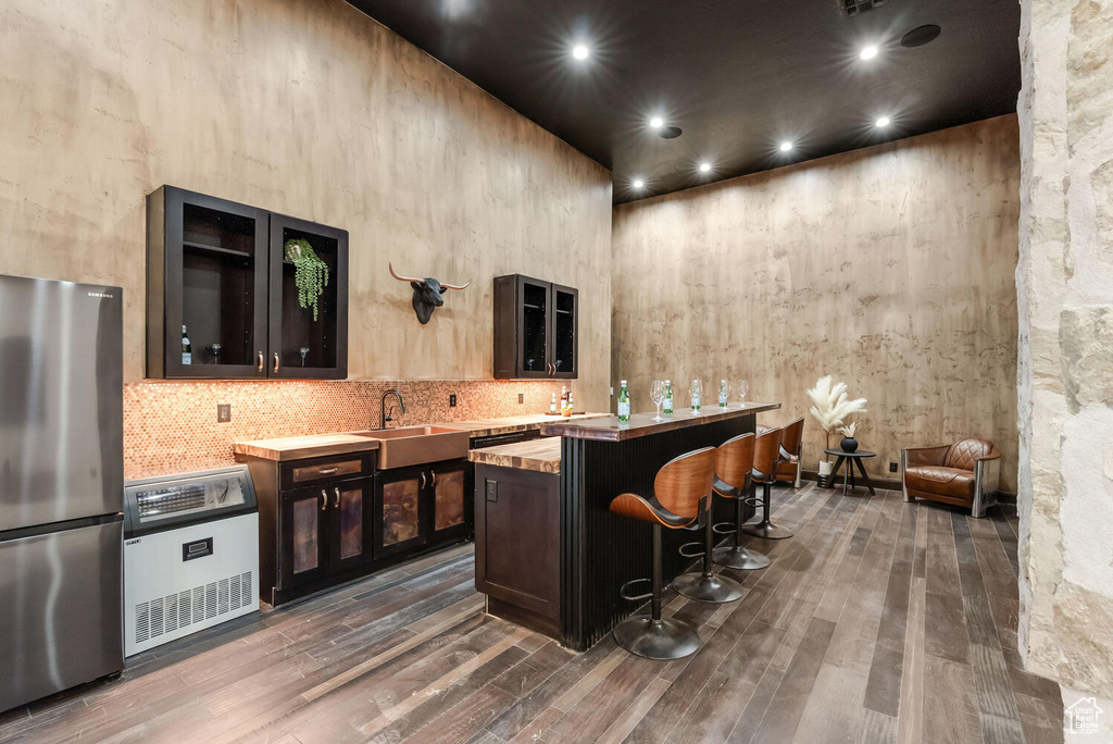 Bar featuring freestanding refrigerator, a sink, dark wood-style flooring, tasteful backsplash, and a towering ceiling