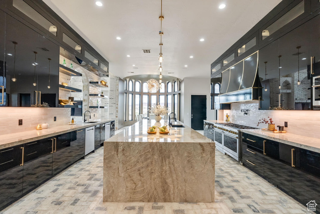 Kitchen featuring appliances with stainless steel finishes, dark cabinets, brick floors, tasteful backsplash, and a sink