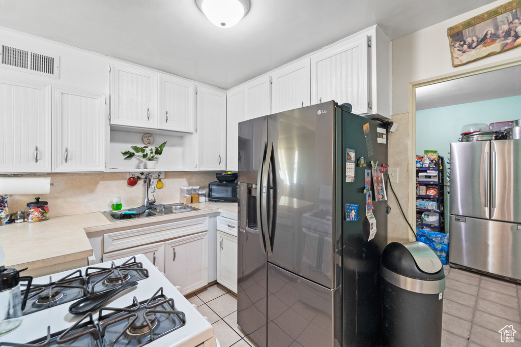 Kitchen featuring freestanding refrigerator, stainless steel refrigerator with ice dispenser, gas range, light countertops, and light tile patterned floors