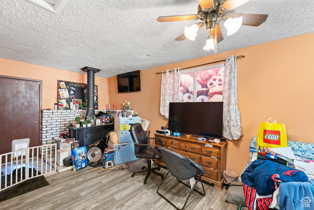 Office featuring wood finished floors, a textured ceiling, a ceiling fan, and a wood stove