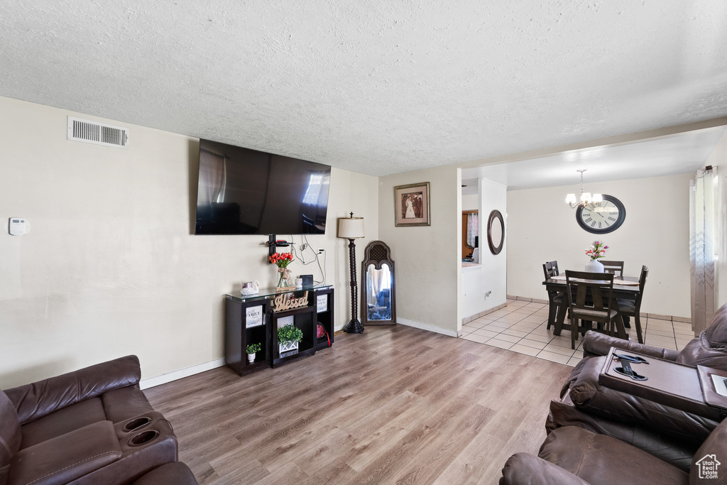 Living room featuring a chandelier, a textured ceiling, light wood-style flooring, and baseboards
