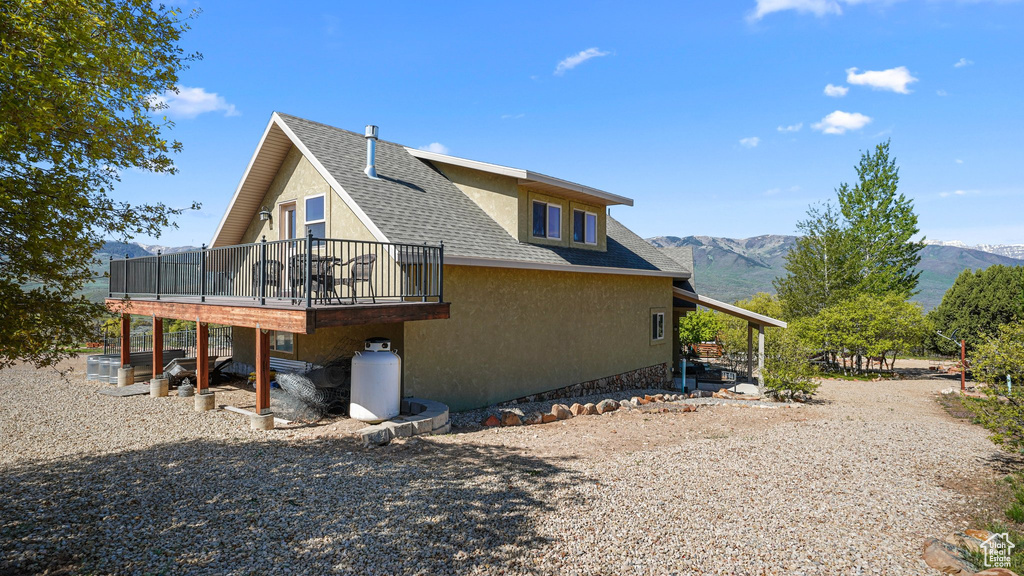 Rear view of house with a shingled roof, stucco siding, and a deck with mountain view