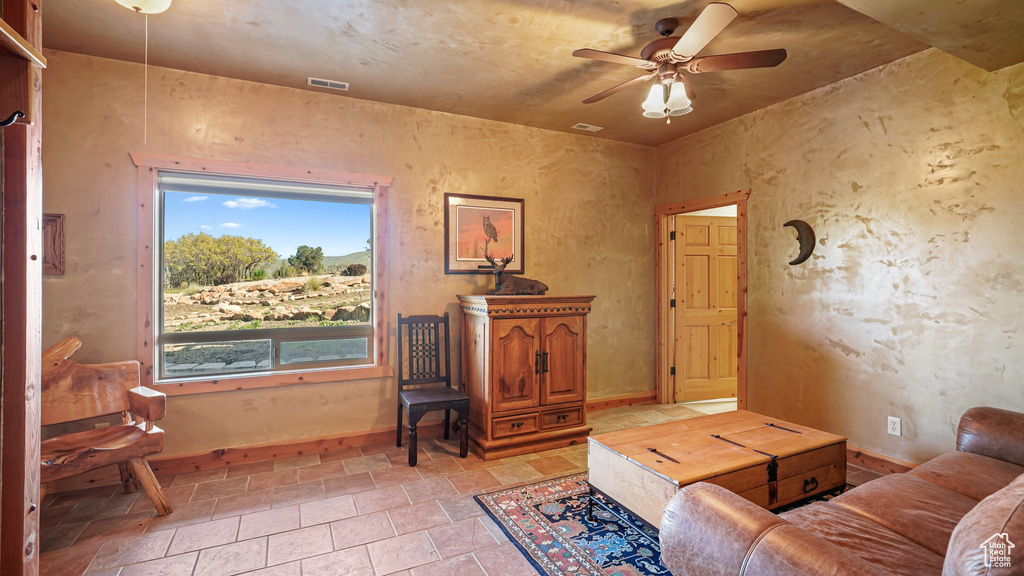 Living area with ceiling fan, baseboards, and light stone finish floors