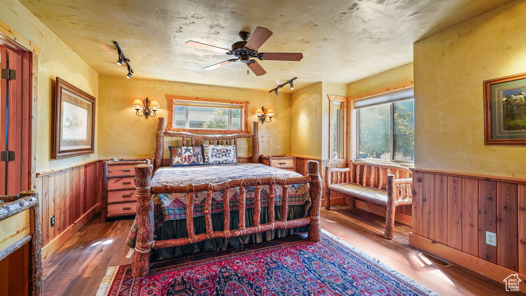 Bedroom with track lighting, a wainscoted wall, hardwood / wood-style flooring, multiple windows, and wooden walls