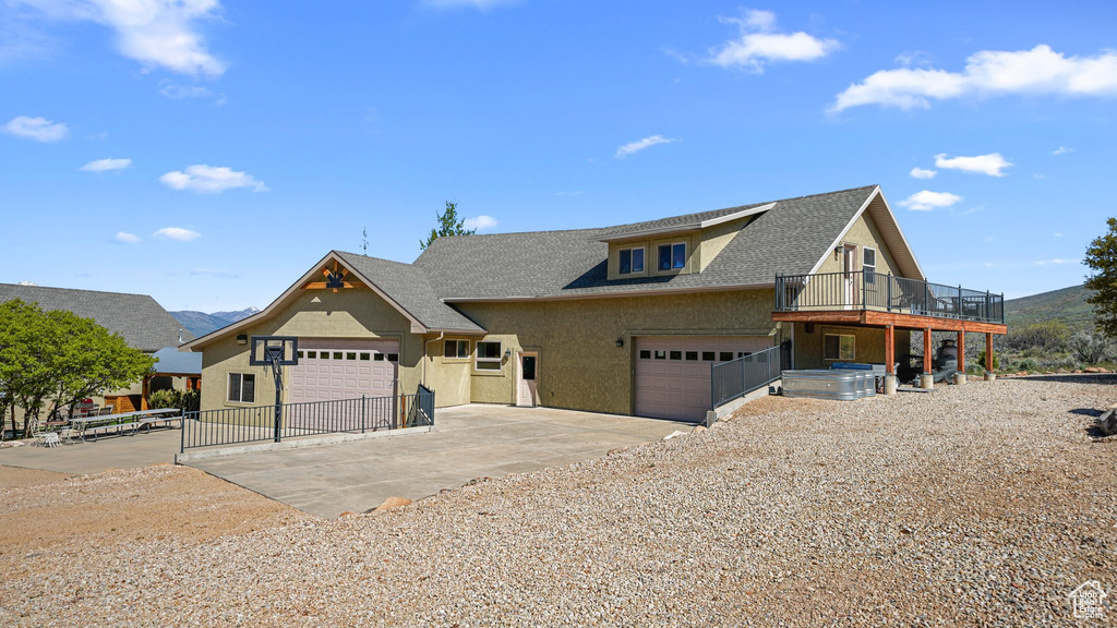 View of front facade featuring driveway, an attached garage, stucco siding, roof with shingles, and a wooden deck