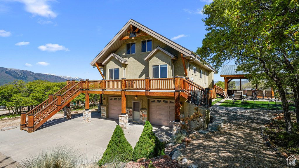 View of front of house with stairs, driveway, stucco siding, a deck with mountain view, and an attached garage