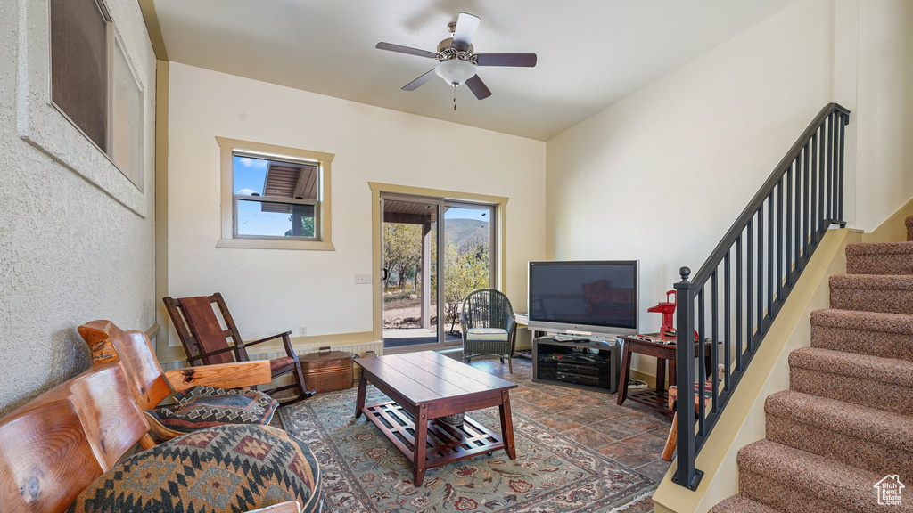 Living room with stairway, a ceiling fan, and stone finish floors