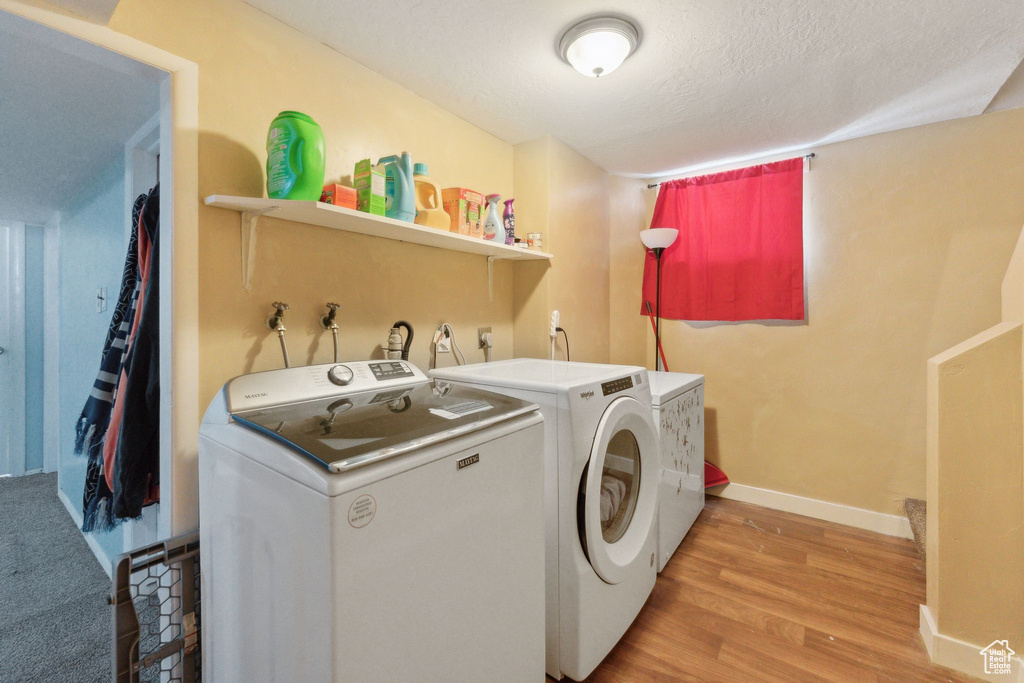Laundry area with washer and clothes dryer, baseboards, light wood-style floors, and a textured ceiling