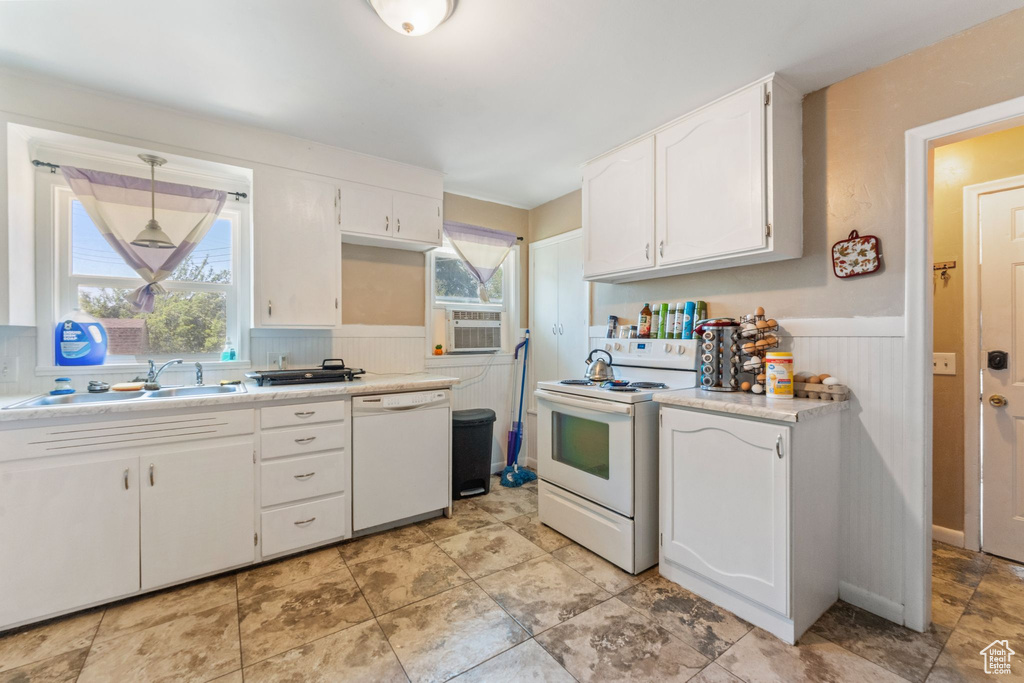 Kitchen with white appliances, a sink, a wainscoted wall, white cabinetry, and light countertops