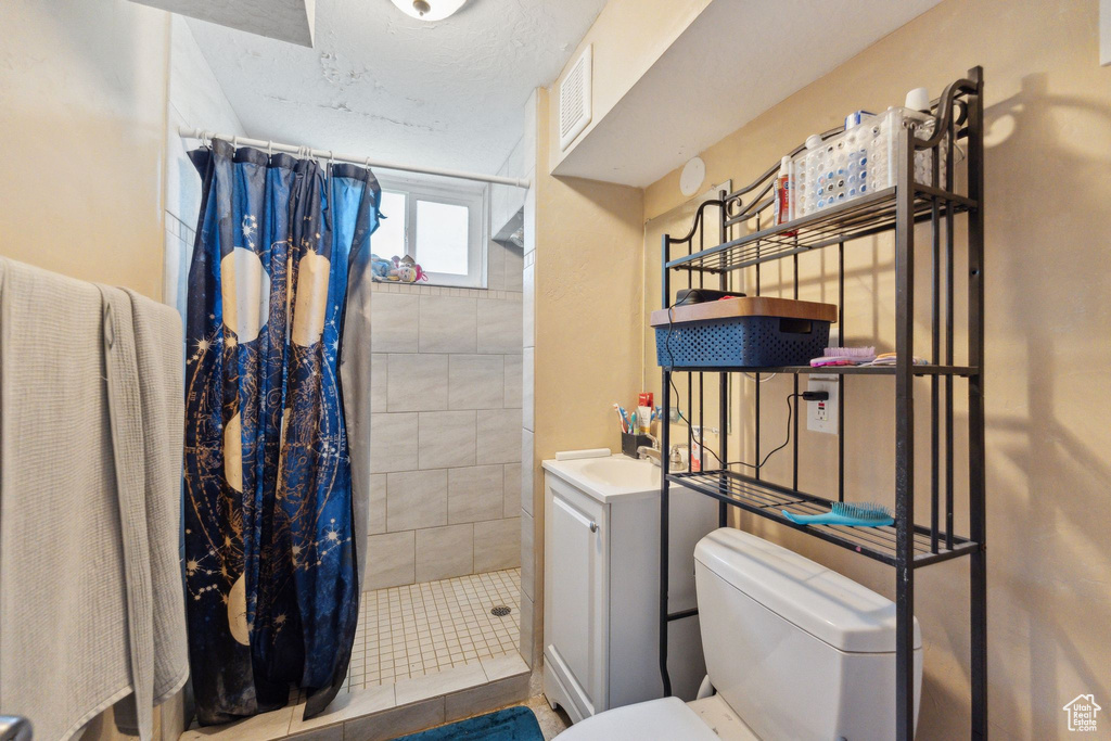 Full bath with toilet, tiled shower, and vanity