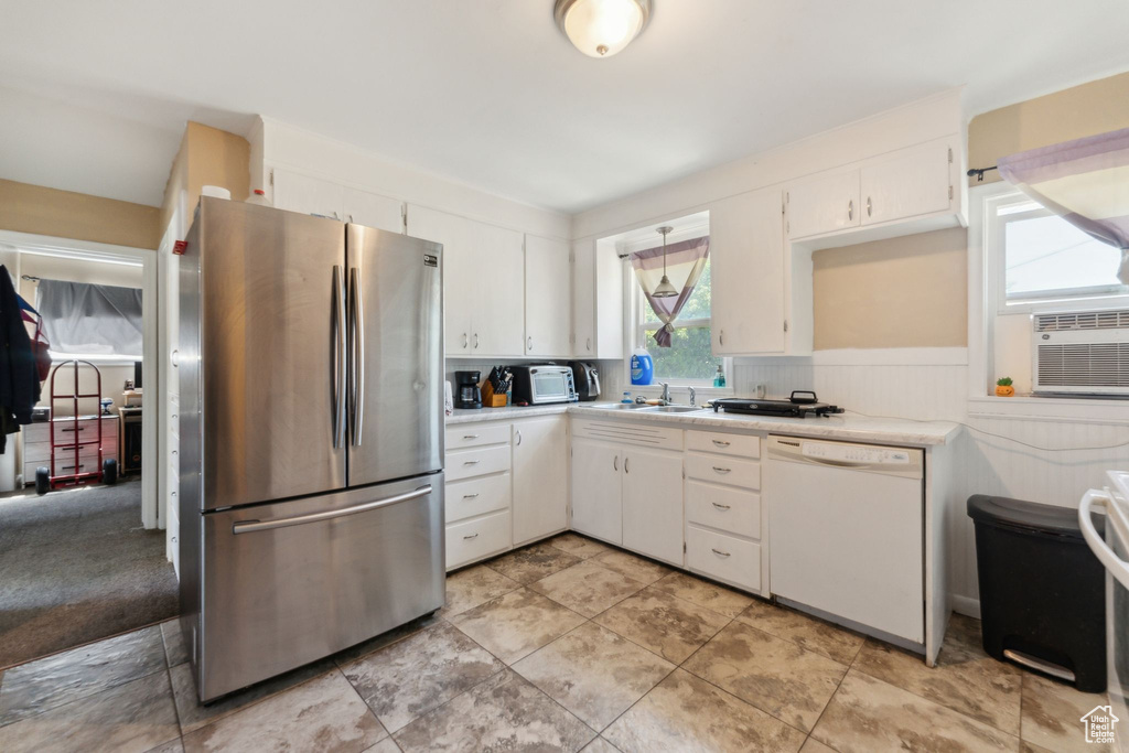 Kitchen with freestanding refrigerator, white dishwasher, light countertops, white cabinets, and a wainscoted wall