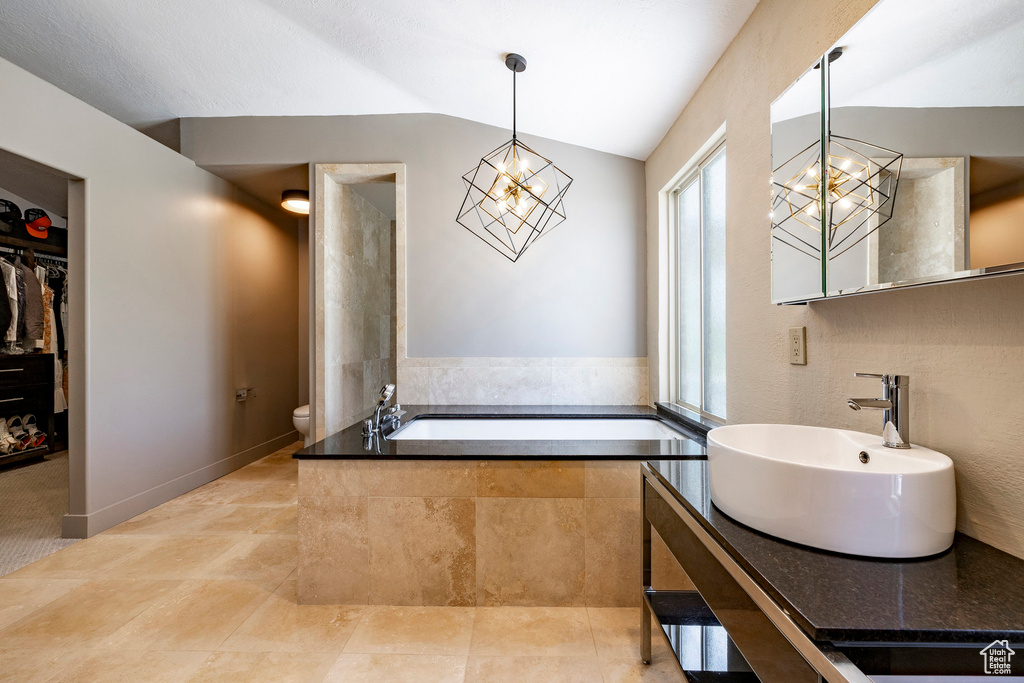 Bathroom featuring a chandelier, toilet, vaulted ceiling, vanity, and a bath