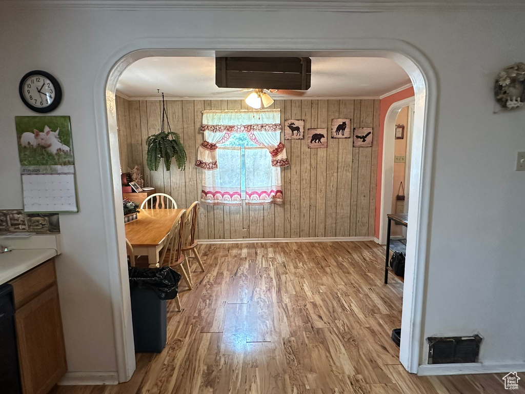 Dining room with arched walkways, light wood-type flooring, baseboards, wooden walls, and a wall unit AC