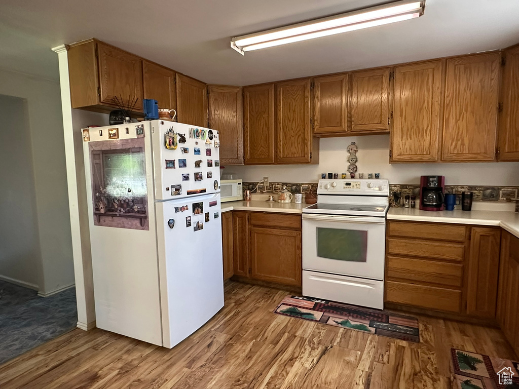 Kitchen featuring white appliances, wood finished floors, brown cabinets, and light countertops
