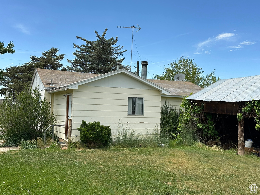 View of side of home with a yard and a shingled roof