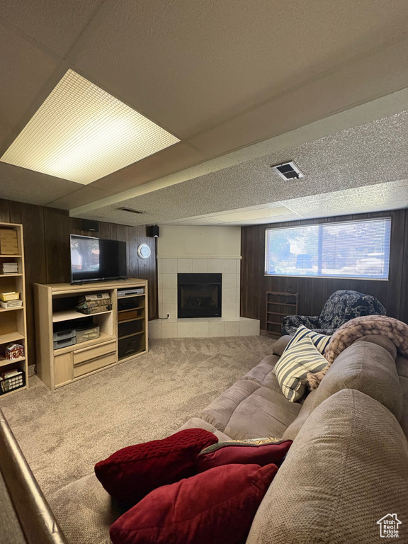 Carpeted living area featuring wooden walls, a tile fireplace, and a textured ceiling